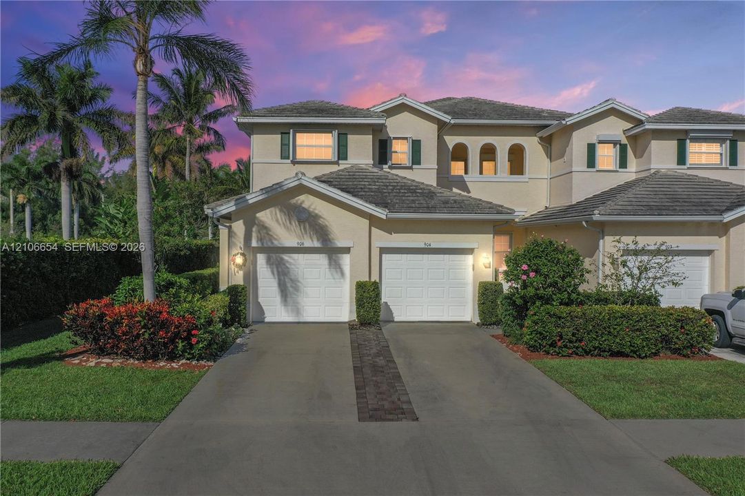Stucco exterior featuring two garage bays, concrete driveway, arched window detailing, and manicured landscaping
