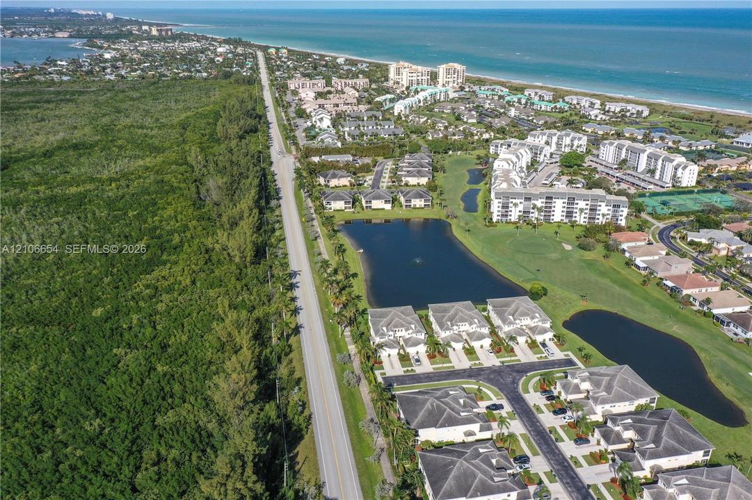 Aerial perspective of a coastal community featuring multi-family residential structures, a freshwater pond, surrounding green space, and proximity to the shoreline