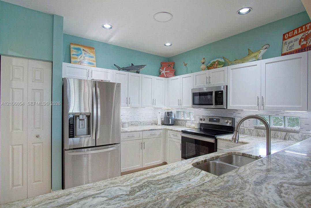 Kitchen featuring white cabinetry, stone countertops, stainless steel appliances, a double-basin stainless steel sink with a pull-down faucet, and recessed lighting