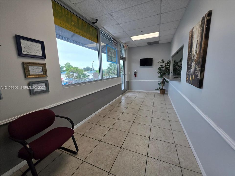 Commercial space featuring large glass storefront windows, neutral ceramic tile flooring, two-tone wall finish with chair rail molding, and a service window