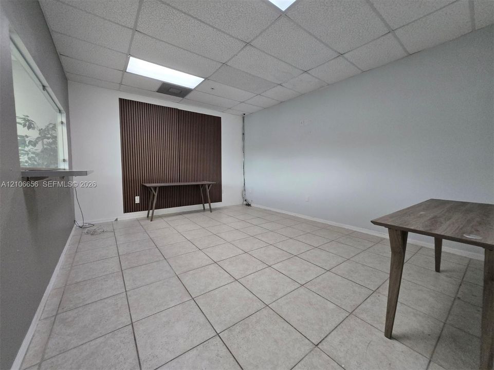 Room featuring neutral tile flooring, a suspended acoustic tile ceiling with recessed lighting, an interior transaction window, and a vertical wood-slat wall accent