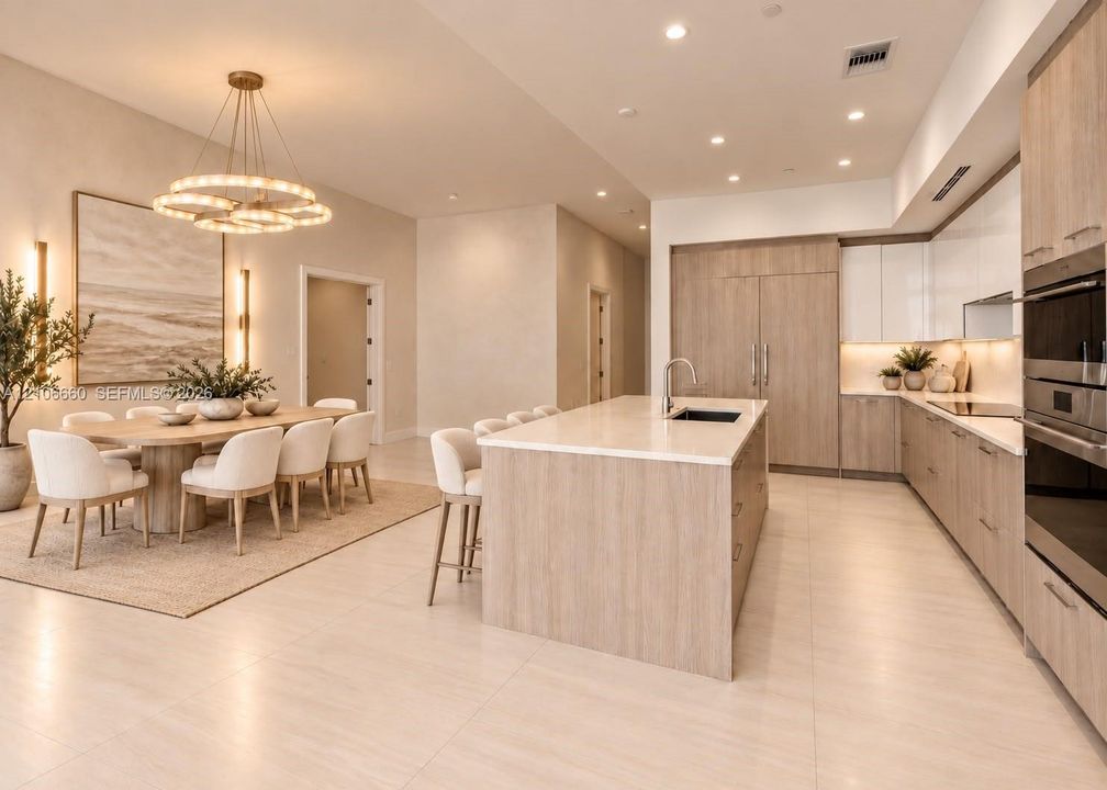 Kitchen featuring light wood-finish cabinetry, a large central island with light-toned countertops, integrated stainless steel appliances, recessed lighting, and a multi-tiered circular chandelier