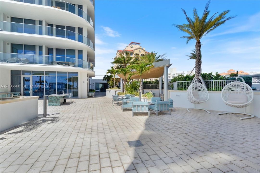 Expansive paved terrace featuring a custom outdoor kitchen with tiled base, metal pergola, and perimeter glass balcony railings