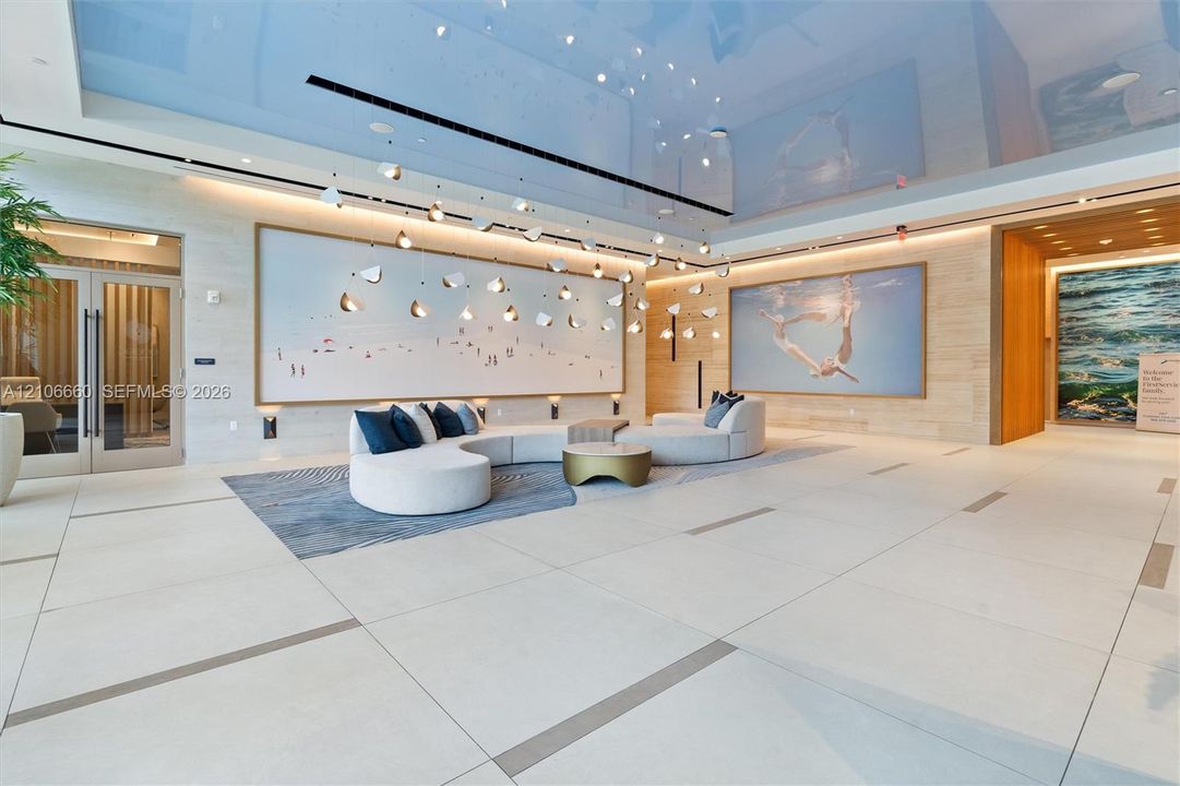 Lobby area featuring large-format tile flooring, a high-gloss reflective ceiling, recessed linear lighting, and integrated wall-mounted fixtures