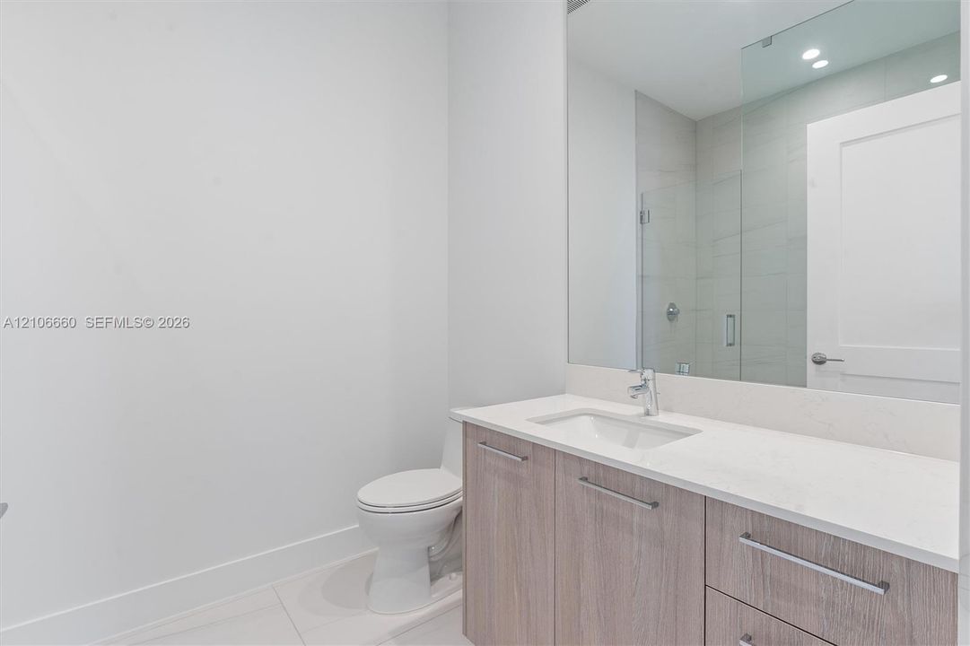 Bathroom featuring a vanity with wood-finish cabinetry, light-toned countertop, undermount sink, large wall-mounted mirror, and glass-enclosed shower