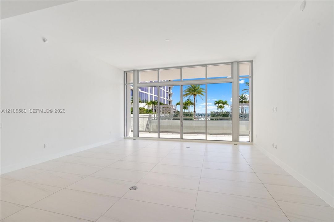Open-concept interior featuring large-format tile flooring, floor-to-ceiling glass wall, and sliding glass doors leading to an exterior balcony