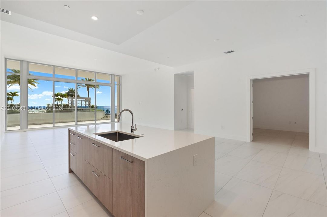 Kitchen island featuring stone countertops, a stainless steel undermount sink, and wood-finish cabinetry, set against large floor-to-ceiling windows with tiled flooring