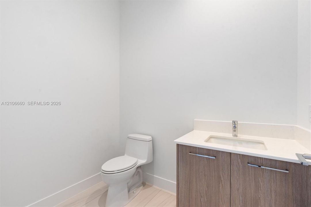 Bathroom featuring a wood-finish vanity with a stone-composite countertop, integrated rectangular sink, chrome-finish faucet, and a one-piece elongated toilet