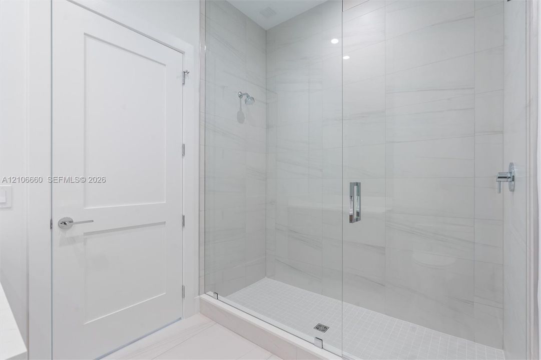 Walk-in shower featuring large-format porcelain tile surround, frameless glass enclosure, polished chrome fixtures, and built-in tiled bench