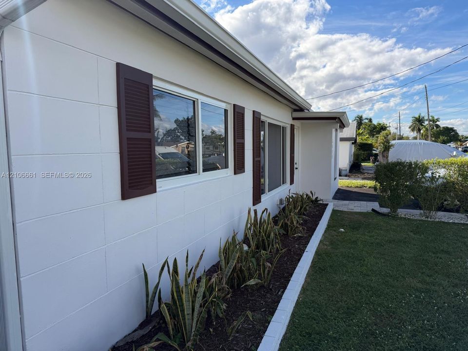 Exterior facade featuring smooth white masonry, decorative brown shutters, sliding windows, and a landscaped garden bed with block border
