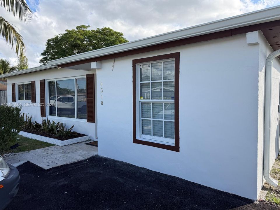 Exterior featuring white stucco finish, contrasting dark-toned window trim and shutters, multi-pane windows, a stone-paved entryway, and built-in stone-edged landscape beds