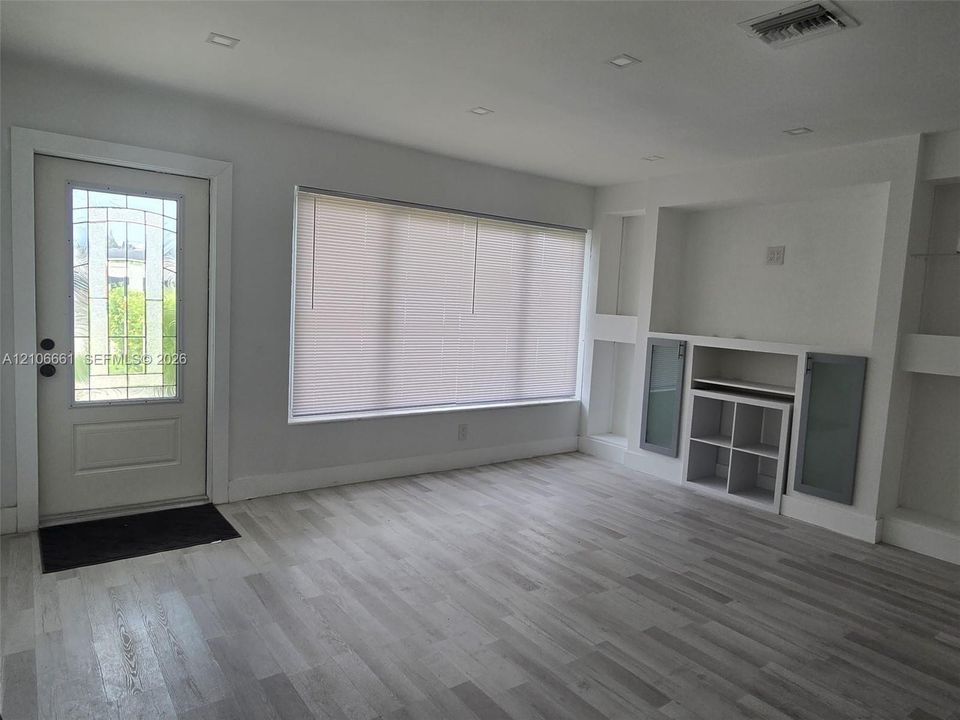 Wood-finish flooring, recessed lighting, large window with integrated blinds, and built-in wall cabinetry featuring glass-front doors