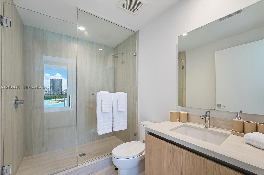 Walk-in shower with floor-to-ceiling tile, frameless glass enclosure, wood-finish cabinetry, countertop vanity with integrated sink, and polished chrome hardware