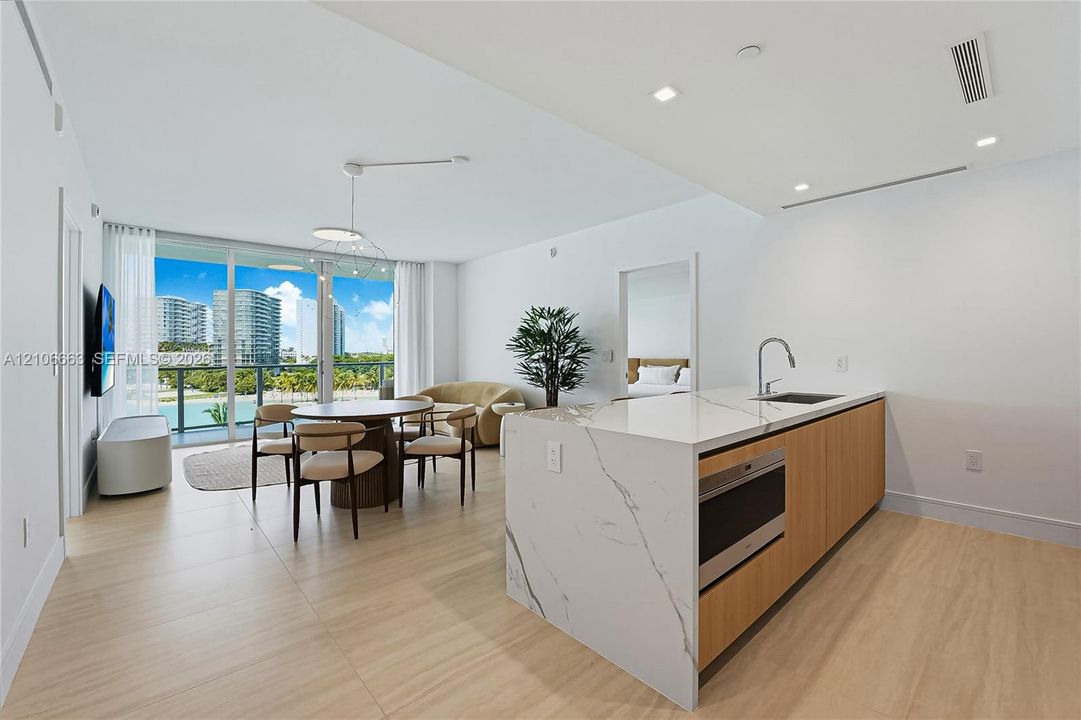 Kitchen island with stone-finish waterfall countertop, wood-finish cabinetry, recessed lighting, wood-finish flooring, and floor-to-ceiling glass sliding doors