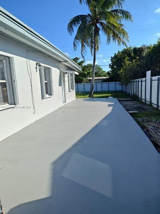 Concrete patio featuring a stucco exterior finish, metal window awnings, and a privacy fence enclosing the backyard