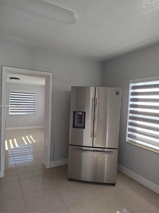 Stainless steel French-door refrigerator, tile flooring, and layered light-filtering window treatments