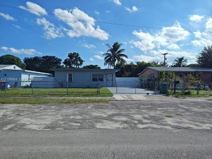 Single-story exterior featuring a concrete driveway, metal chain-link fencing, and a white privacy-style gate