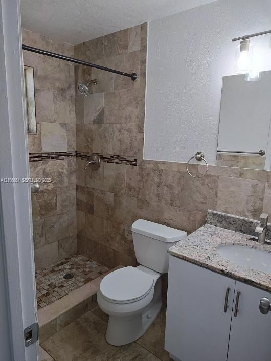 Full bathroom featuring a shower with stone-tile surround and mosaic accent detailing, a stone-composite countertop, vanity cabinetry, and a wall-mounted light fixture