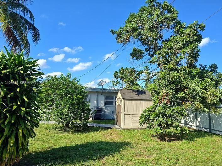 Backyard featuring a grass lawn, mature trees, and a detached resin storage shed