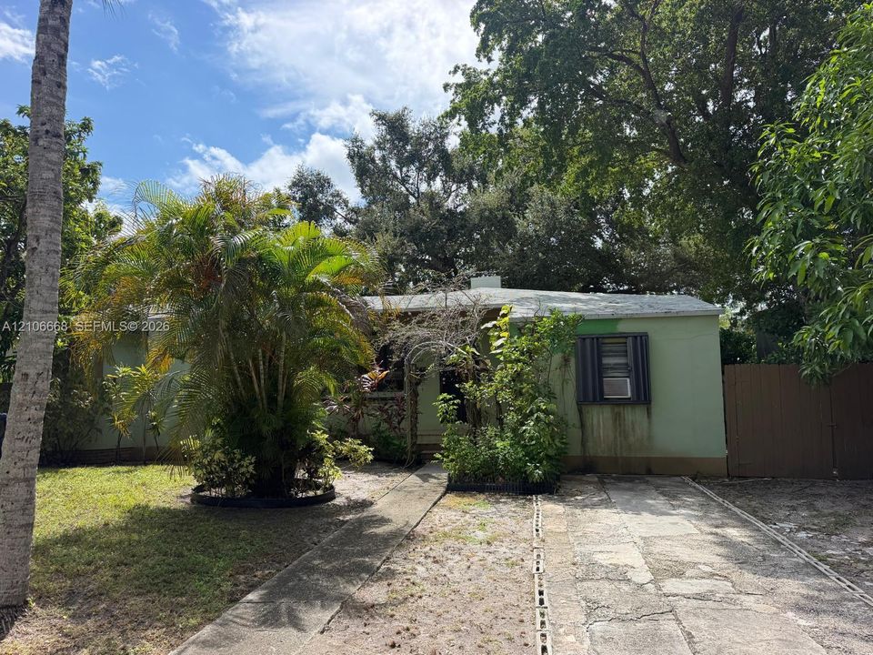 Single-story residence featuring an exterior concrete walkway, paved driveway, exterior shutters, and mature trees