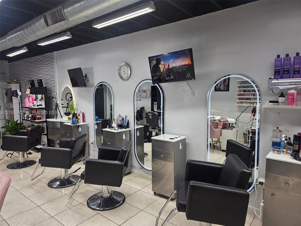 Commercial studio space featuring tile flooring, exposed ductwork, wall-mounted backlit oval mirrors, and stainless steel cabinetry