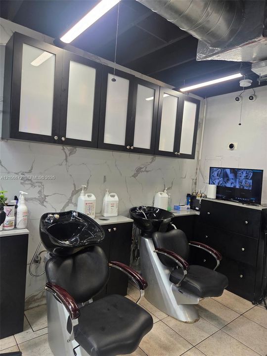 Dedicated workspace featuring stone-patterned wall surfacing, black cabinetry with frosted glass inserts, and dual integrated shampoo basins