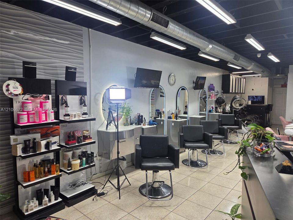 Commercial space featuring exposed industrial-style ductwork, high-contrast black ceiling, textured accent wall, integrated LED-backlit mirrors, and polished tile flooring