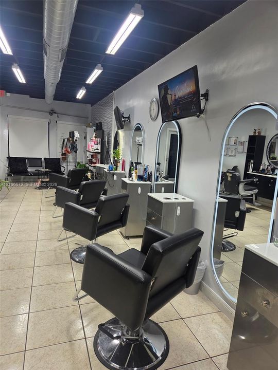 Commercial interior featuring an exposed industrial ceiling, tile flooring, wall-mounted oval LED-backlit mirrors, and integrated cabinetry with stone-finish countertops
