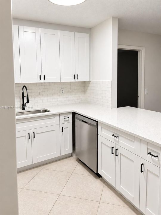 White shaker-style cabinetry with matte black hardware, stone-composite countertops, subway tile backsplash, stainless steel dishwasher, and undermount kitchen sink with a high-arch pull-down faucet
