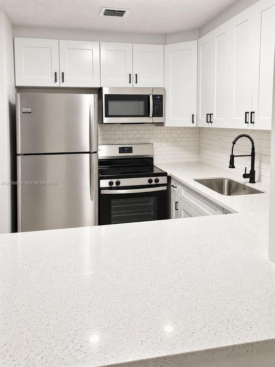 Kitchen featuring white shaker-style cabinetry, stainless steel appliances, quartz countertops, a white subway tile backsplash, and a matte black gooseneck faucet