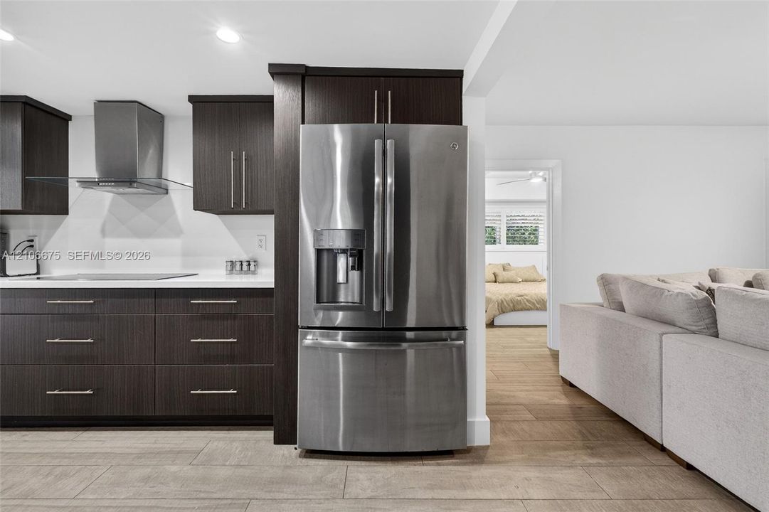 Dark wood-finish cabinetry, stainless steel French-door refrigerator, integrated chimney-style range hood, solid-surface countertops, and wood-finish flooring