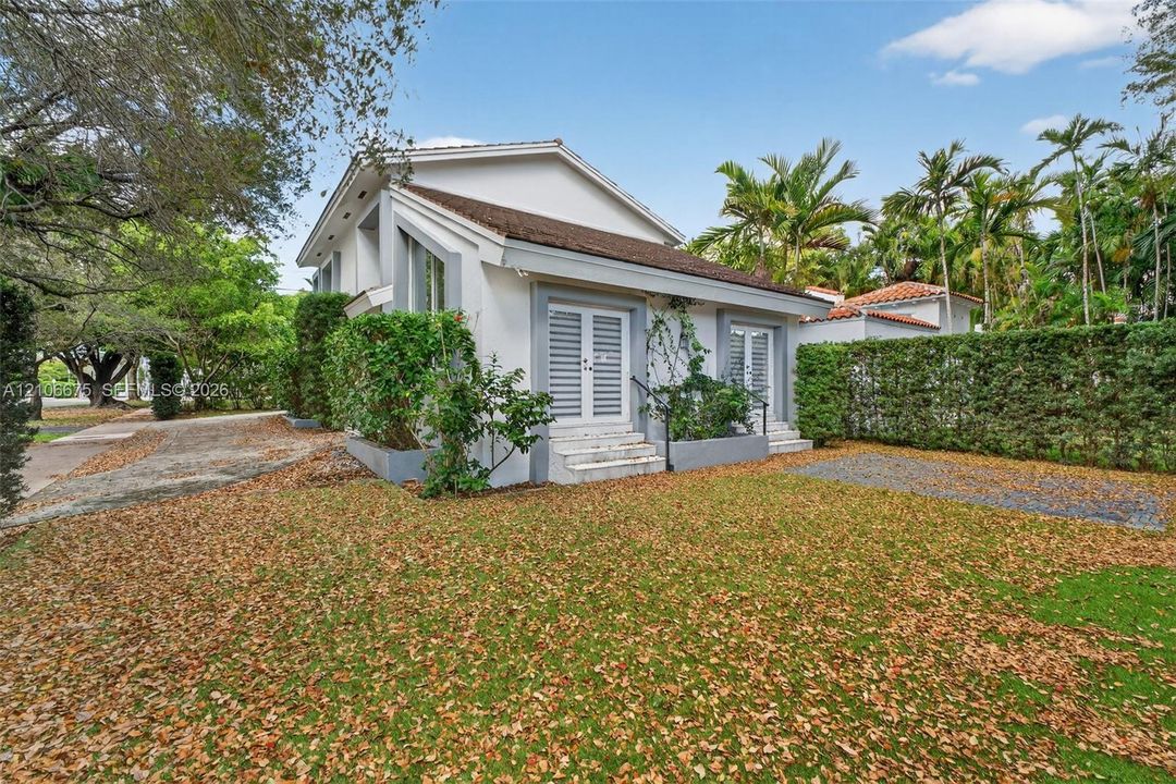 Exterior featuring white stucco facade, dual sets of louvered French doors, tiered entryway steps, pitched shingle roof, and established perimeter hedges