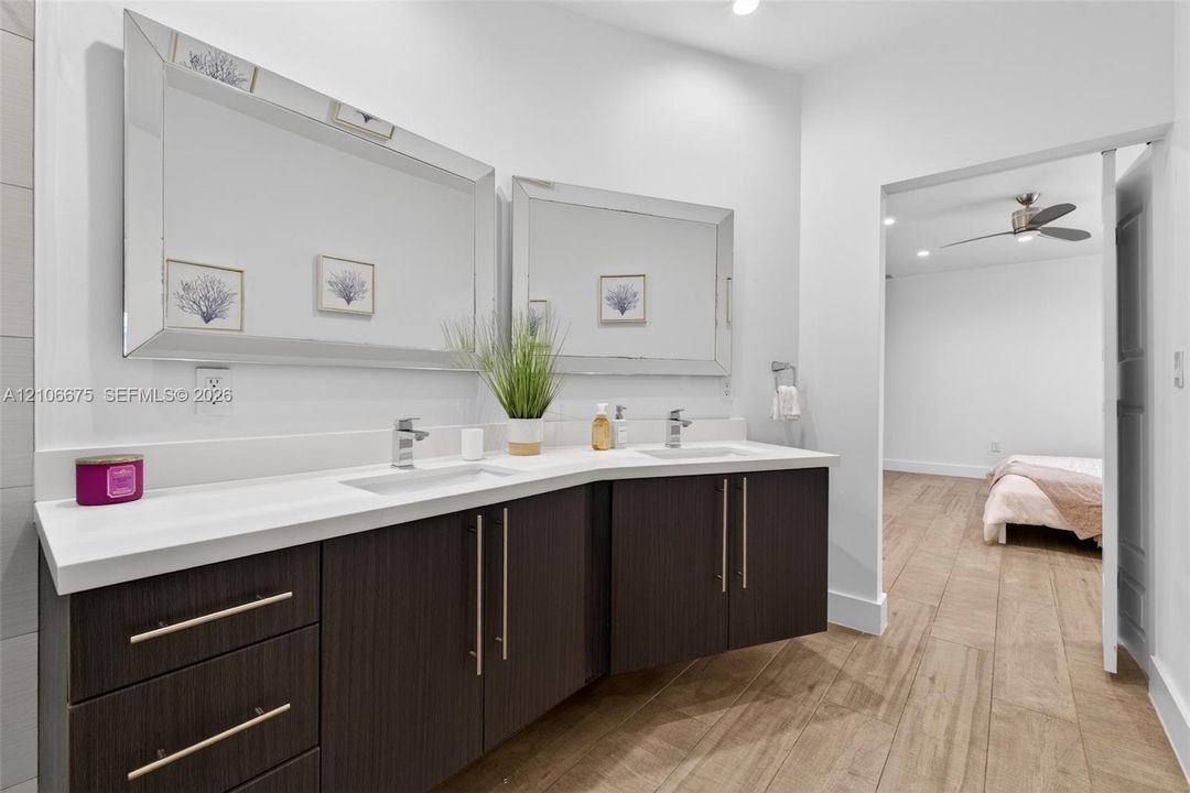 Floating vanity featuring dark wood-finish cabinetry, dual under-mount sinks, light-toned stone-style countertop, and beveled-edge wall mirrors