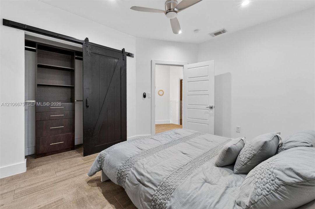Bedroom featuring wood-finish flooring, a ceiling fan, and a walk-in closet with built-in dark wood cabinetry behind a sliding black barn door