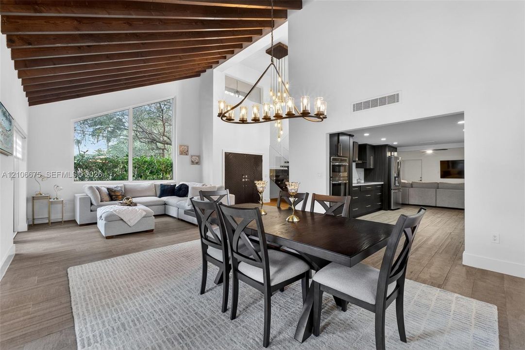 Vaulted ceiling with exposed wood beams, oversized picture window, wood-finish tile flooring, and multi-light industrial-style chandelier