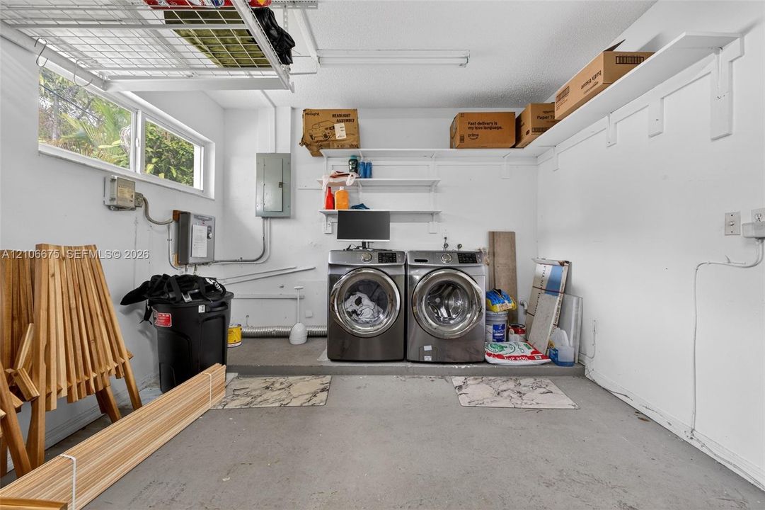 Garage utility area featuring wall-mounted open shelving, overhead wire storage rack, horizontal slider window, and laundry hookups