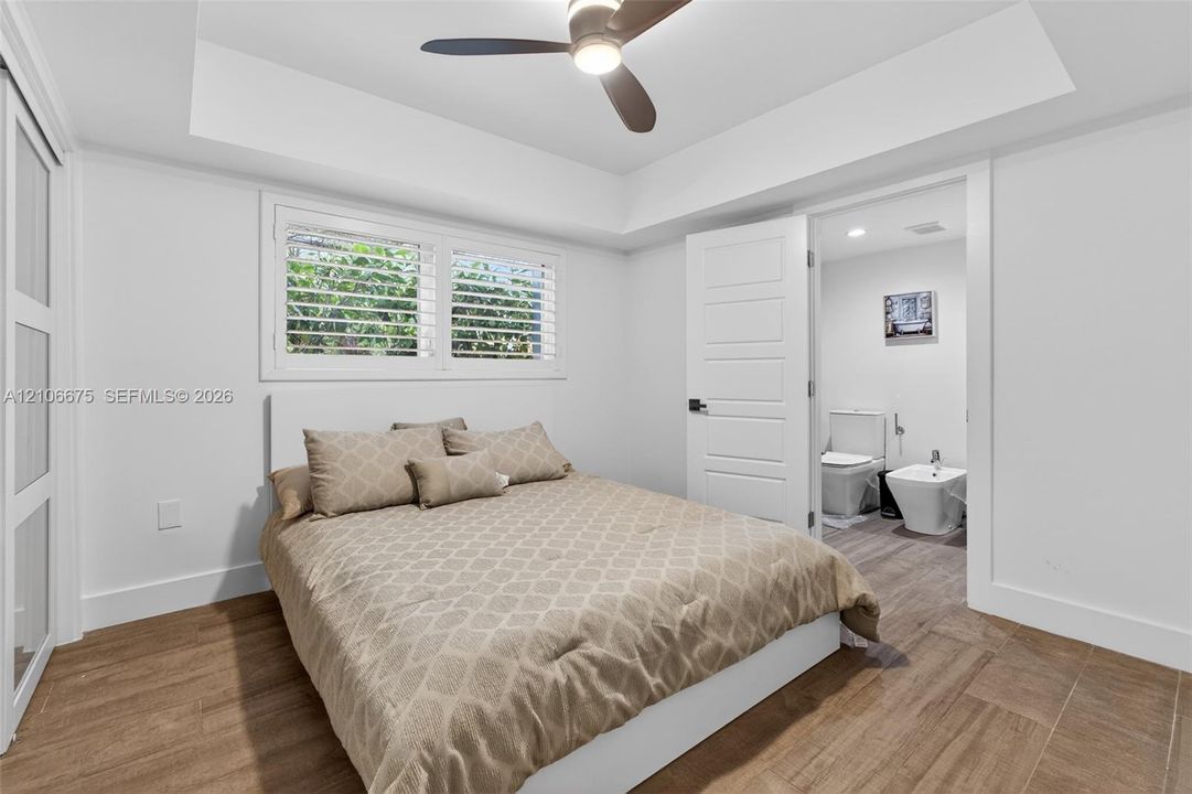 Tray ceiling with integrated lighting, wood-finish tile flooring, shutter-style window coverings, and a ceiling fan