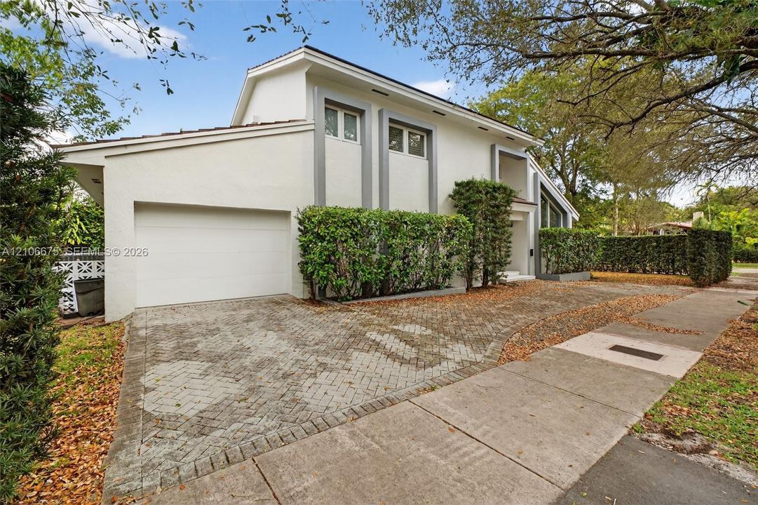 Contemporary two-story exterior featuring a smooth stucco facade, herringbone-patterned paver driveway, multi-level roofline, and integrated landscaping