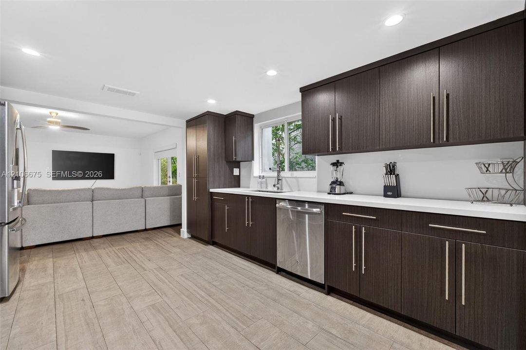 Kitchen featuring dark-toned cabinetry, stainless steel appliances, white solid-surface countertops, and wood-finish flooring
