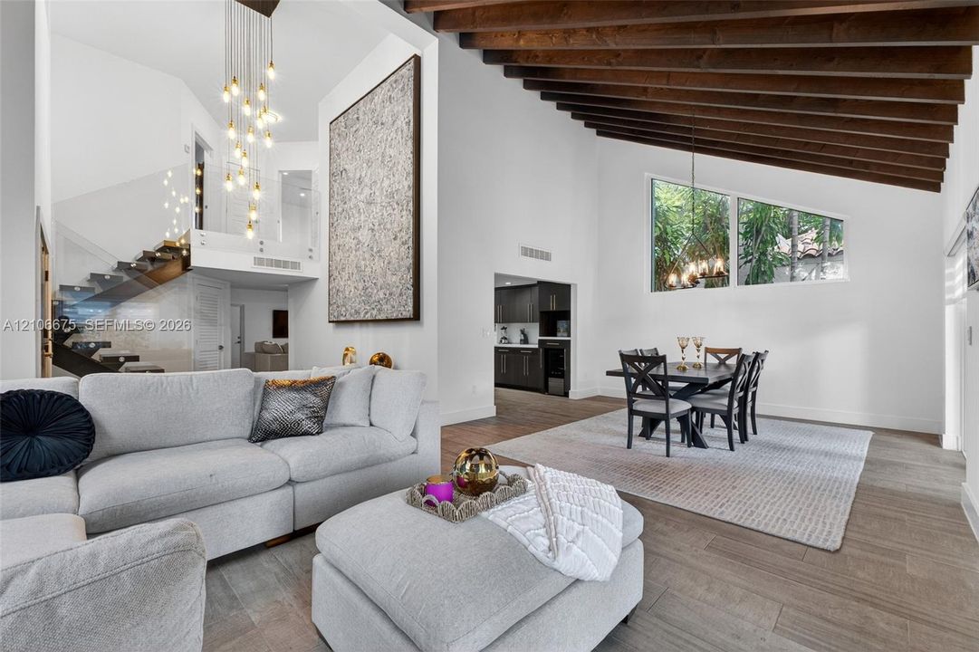 Vaulted ceilings with exposed wood beams, wood-finish flooring, glass-paneled staircase railing, multi-tier pendant lighting, and oversized trapezoidal windows