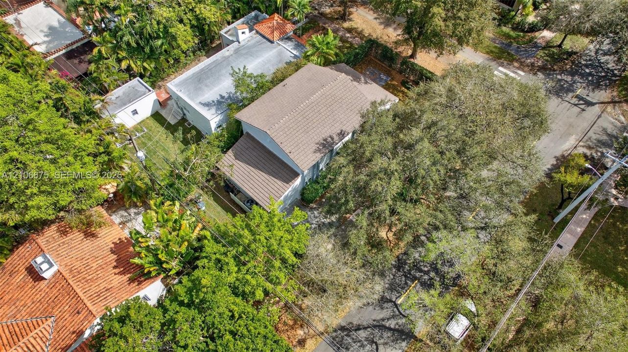 Aerial perspective of a multi-level structure featuring a tile roof, paved driveway, and mature landscaping with extensive tree canopy coverage