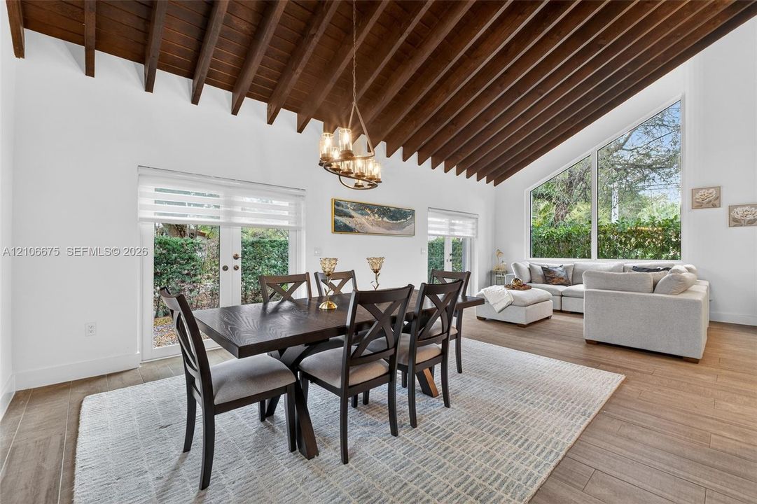 Vaulted ceiling with exposed wooden beams, wood-finish flooring, floor-to-ceiling angled window, and double glass-paned doors