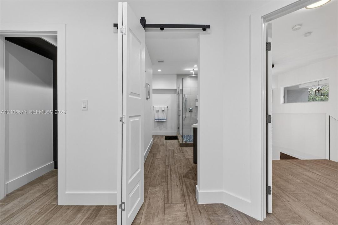 Wood-finish tile flooring, black metal sliding barn door hardware, multi-panel interior doors, recessed lighting, and glass-enclosed shower