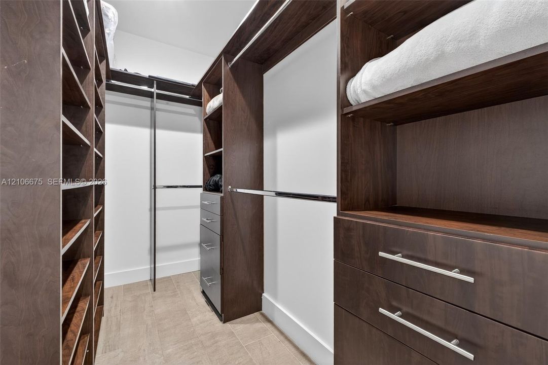 Walk-in closet featuring custom wood-finish cabinetry, built-in shelving, integrated dresser drawers with metallic hardware, and overhead hanging rods