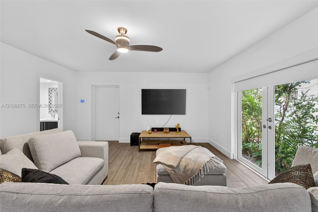 Neutral-toned interior space featuring wood-finish flooring, a modern multi-blade ceiling fan with integrated lighting, and full-height glass French doors