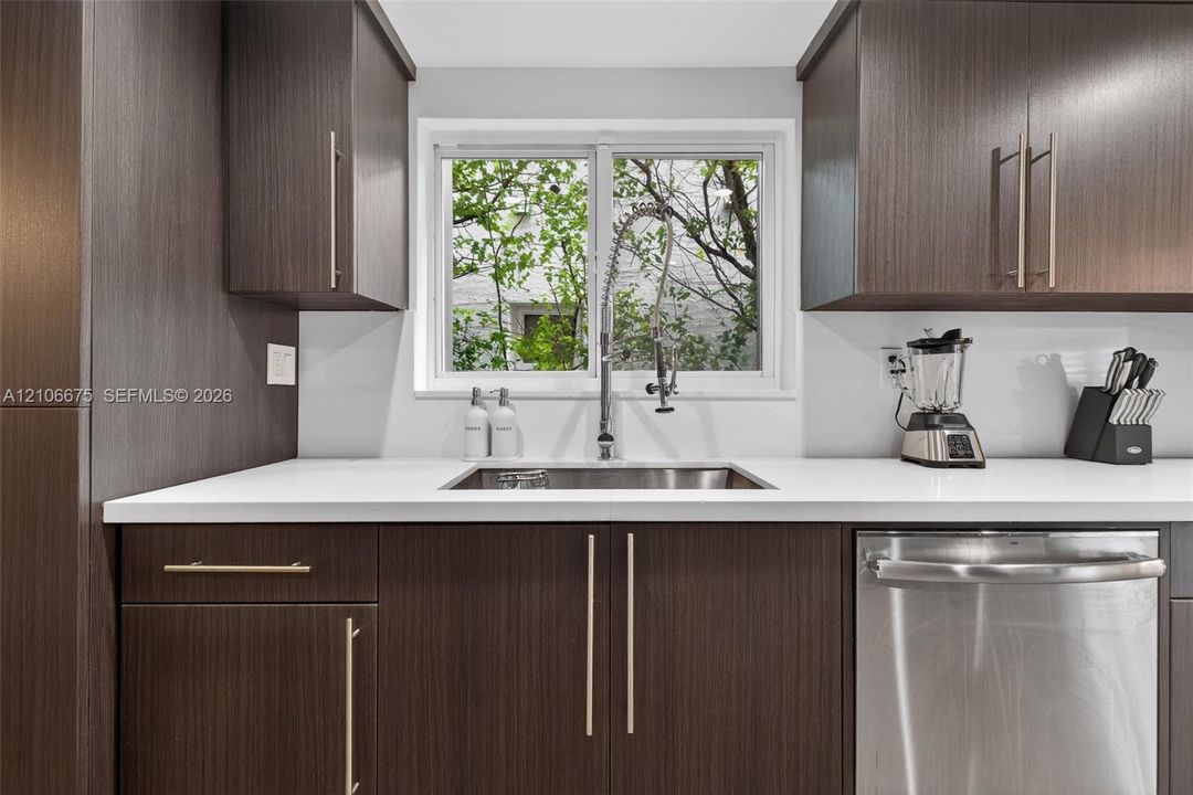 Kitchen featuring dark wood-finish cabinetry, solid-surface countertops, a stainless steel undermount sink, a gooseneck faucet, and a stainless steel dishwasher