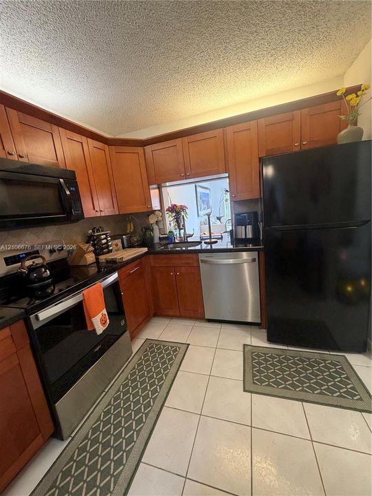 Kitchen featuring medium-toned wood cabinetry, dark stone countertops, tile flooring, and integrated black and stainless steel appliances
