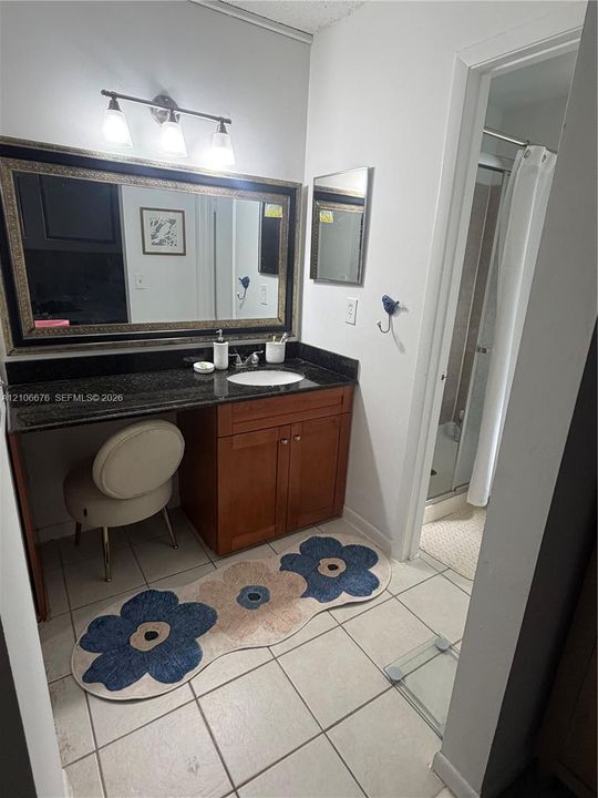 Vanity with stone countertop, integrated oval basin, warm-toned wood cabinetry, large-scale framed mirror, and three-light wall-mounted fixture