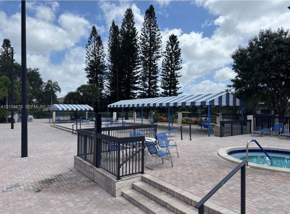 Outdoor area featuring a circular spa, paver patio, blue and white striped shade structures, and metal perimeter fencing