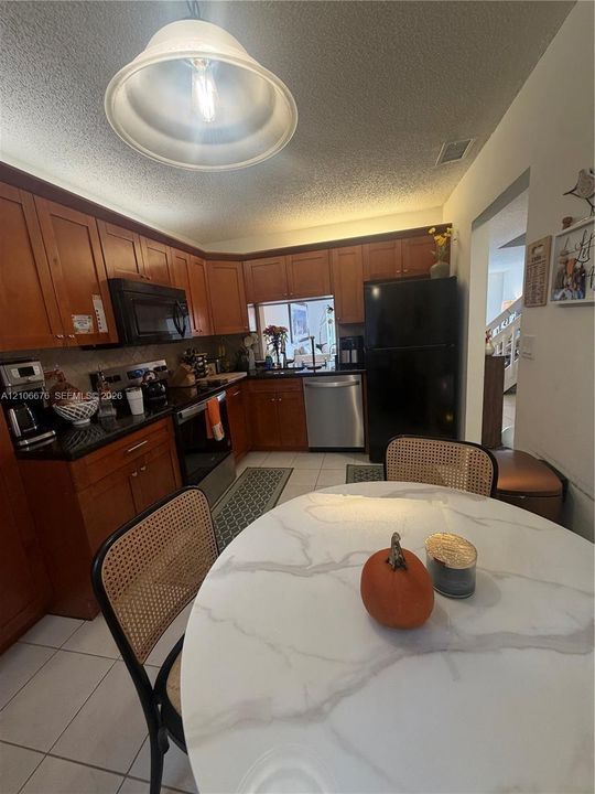 Kitchen featuring wood cabinetry, black solid-surface countertops, stainless steel appliances, and tile flooring